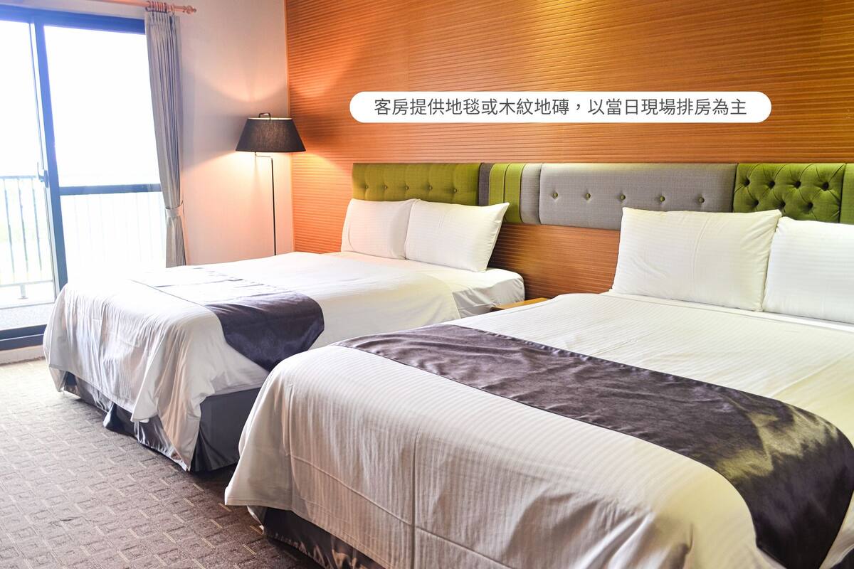 A hotel room with two beds, a wooden headboard, and a large window with curtains.