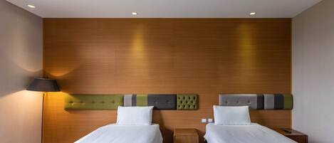 A hotel room with two beds, a wooden headboard, a bedside table, and a lamp.