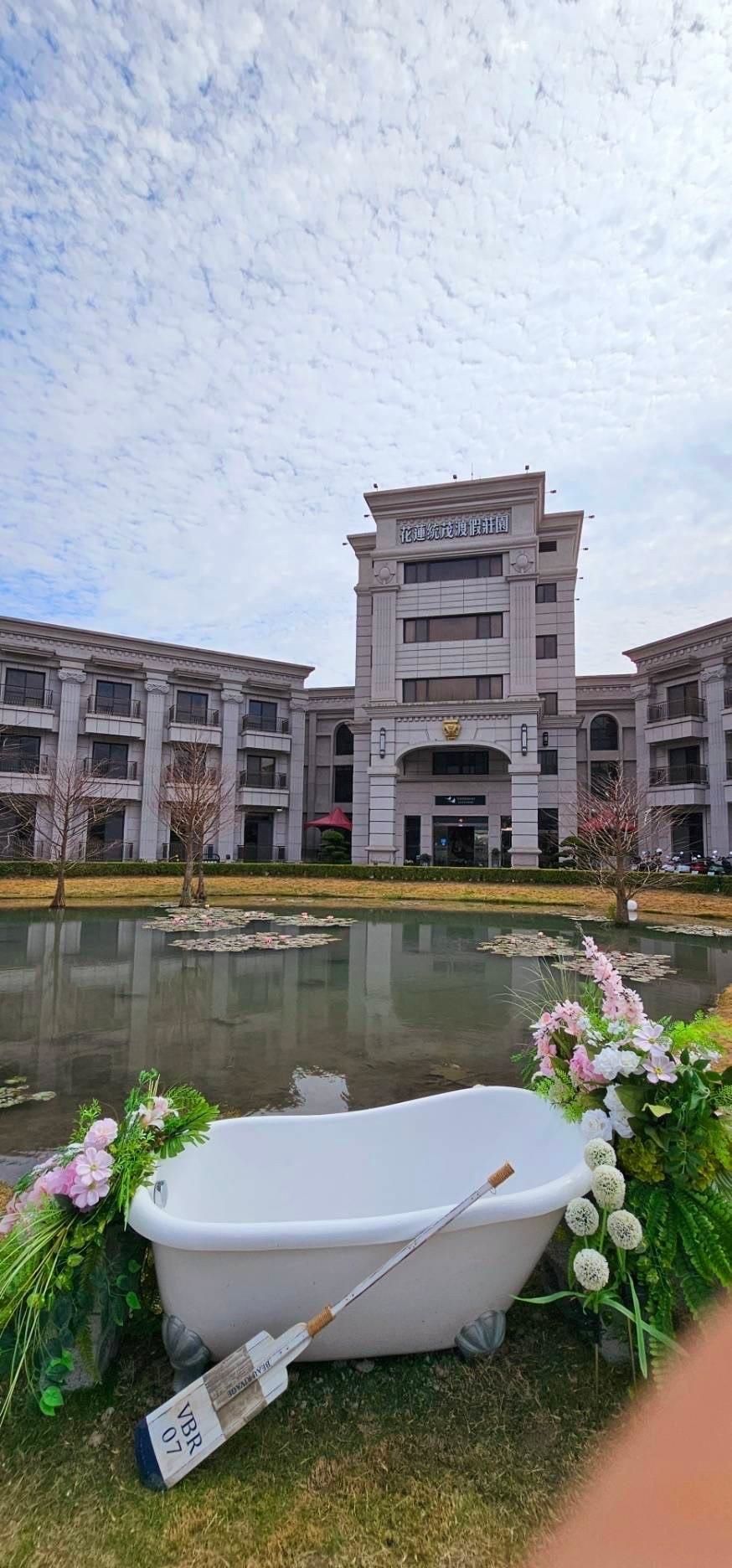 A building with a classical architectural style, a pond with lily pads, and a white bathtub with a label.