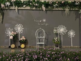 Un escenario con un mensaje, estructuras decorativas parecidas a dientes de león, una silla de metal y plantas en macetas.