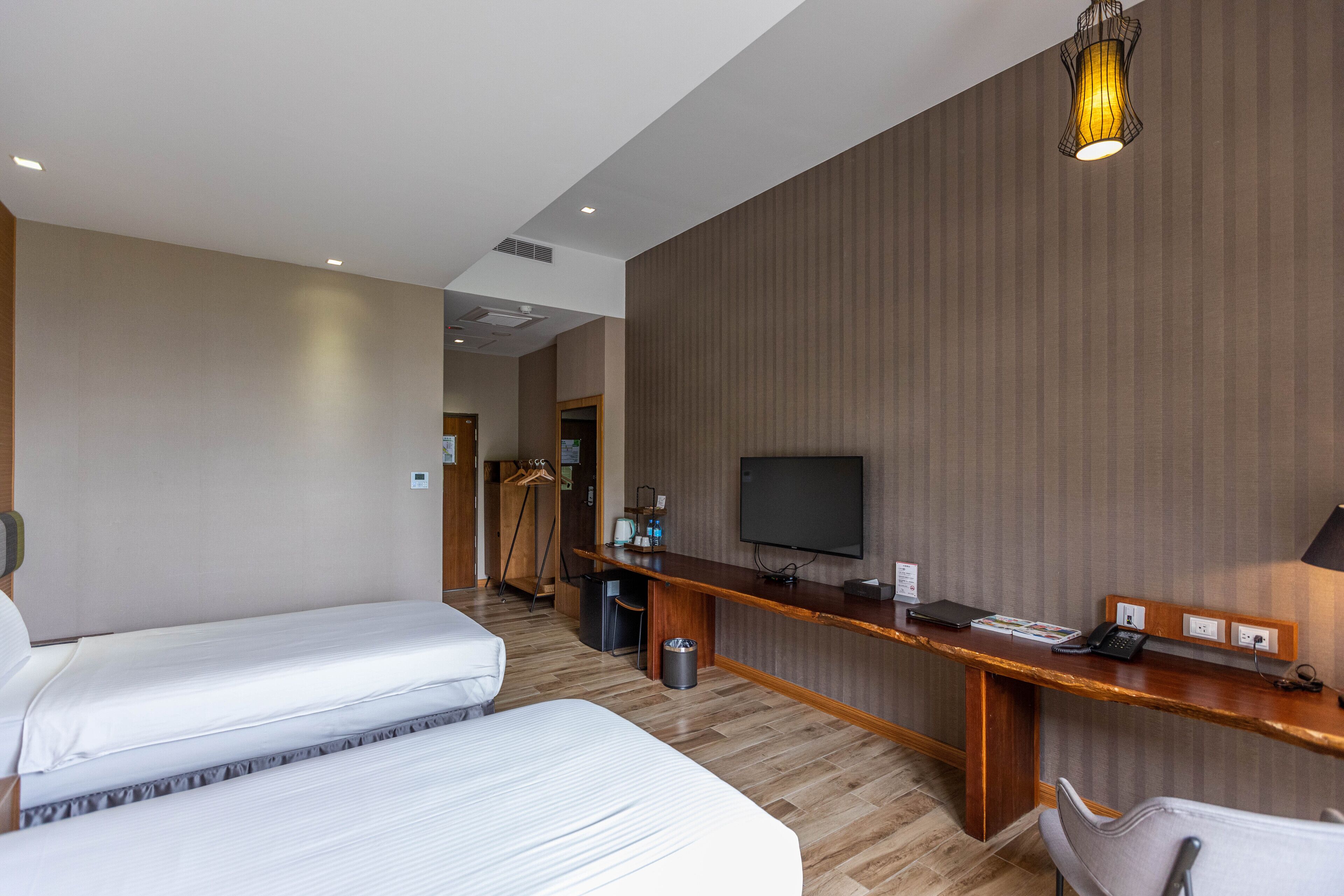Habitación de hotel con dos camas, un escritorio, un televisor de pantalla plana, un cesto de basura y un perchero.