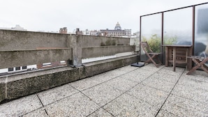 Una terraza en la azotea con un muro de hormigón, una silla de madera y una mesa.