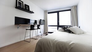 Una habitación de hotel moderna con una cama, un escritorio con dos sillas, un televisor y una ventana con cortinas.