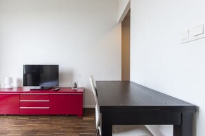 Ein Zimmer mit einem schwarzen Tisch, einem roten Schrank mit Fernseher und einem weißen Stuhl.