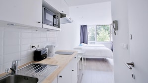 Habitación de hotel compacta con kitchenette, una cama y una ventana con cortinas.