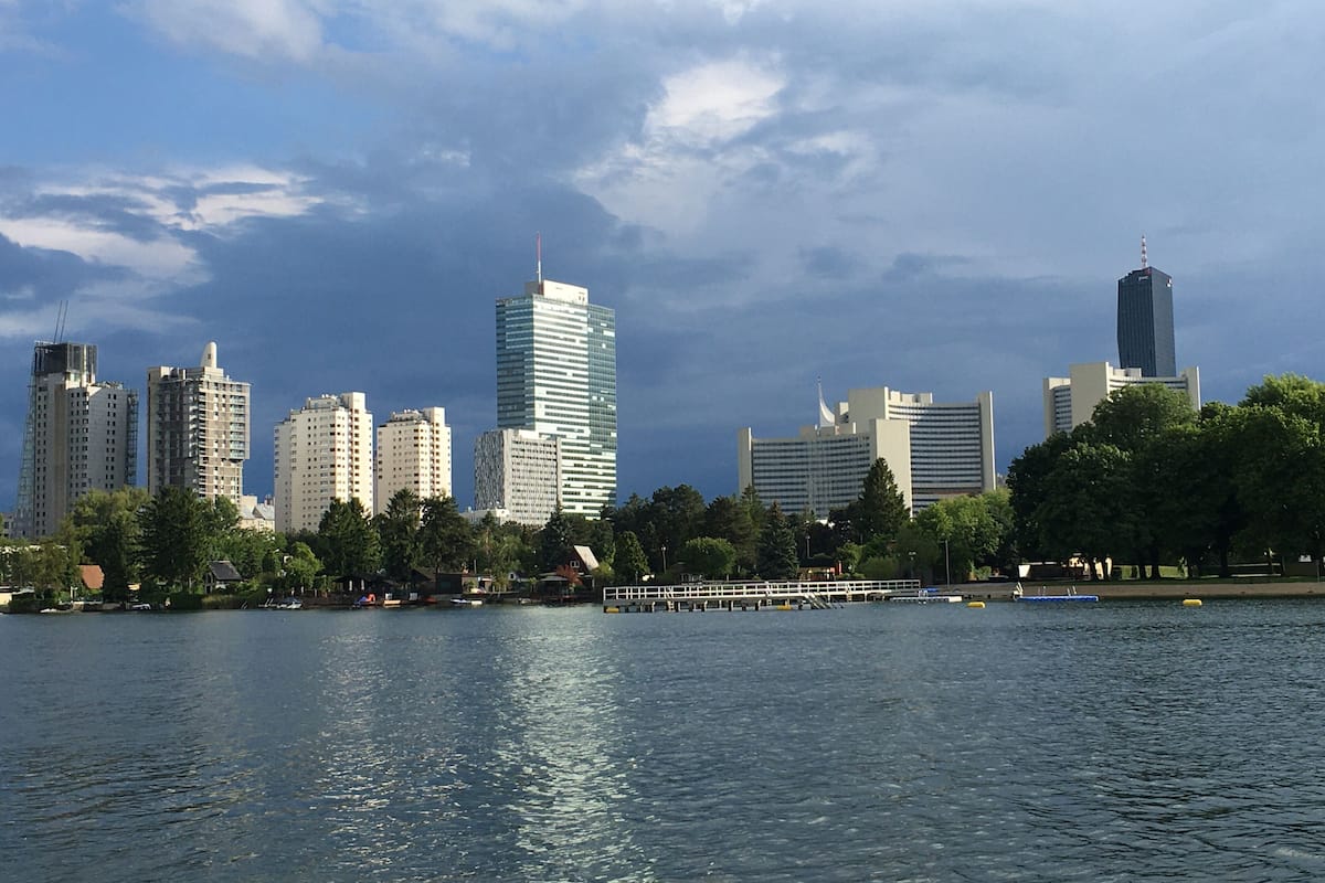 Une vue sur les toits d’une ville, avec des immeubles modernes et des gratte-ciel, et une étendue d’eau au premier plan.