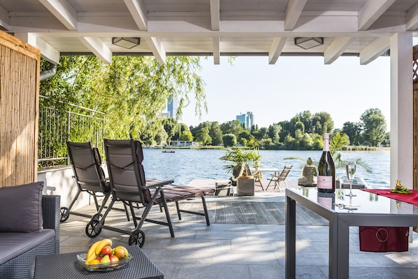 Eine Terrasse mit Seeblick, Sitzgelegenheiten im Freien und einem Tisch mit Flasche und Glas.