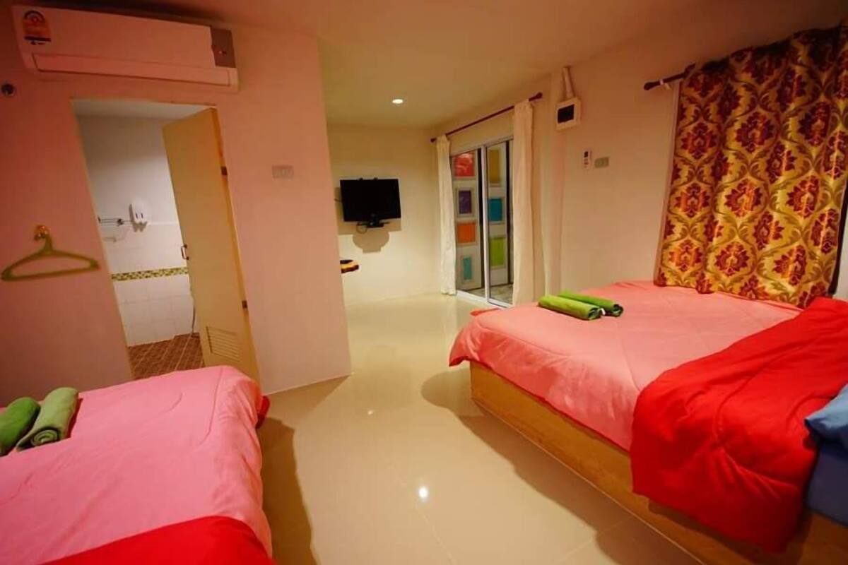 A hotel room with two beds, a television, a bathroom with a shower, and a patterned curtain.