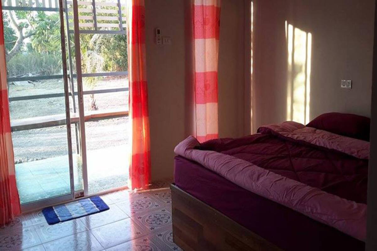 A bedroom with a bed, a sliding glass door leading to an outdoor area, and a window with curtains.