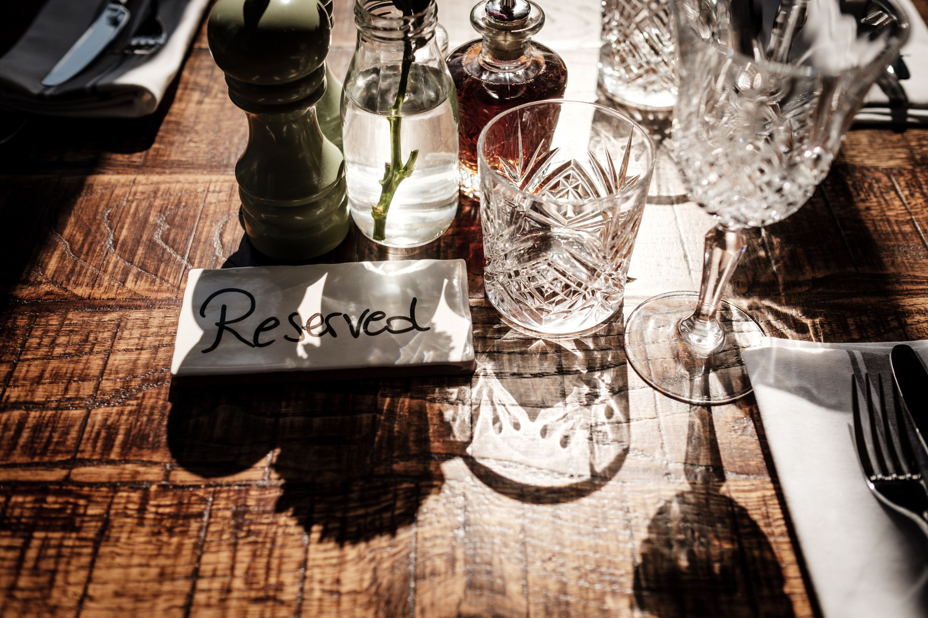 Een tafel gedekt met een 'Gereserveerd'-bordje, helder glaswerk en een zout- en peperstel.