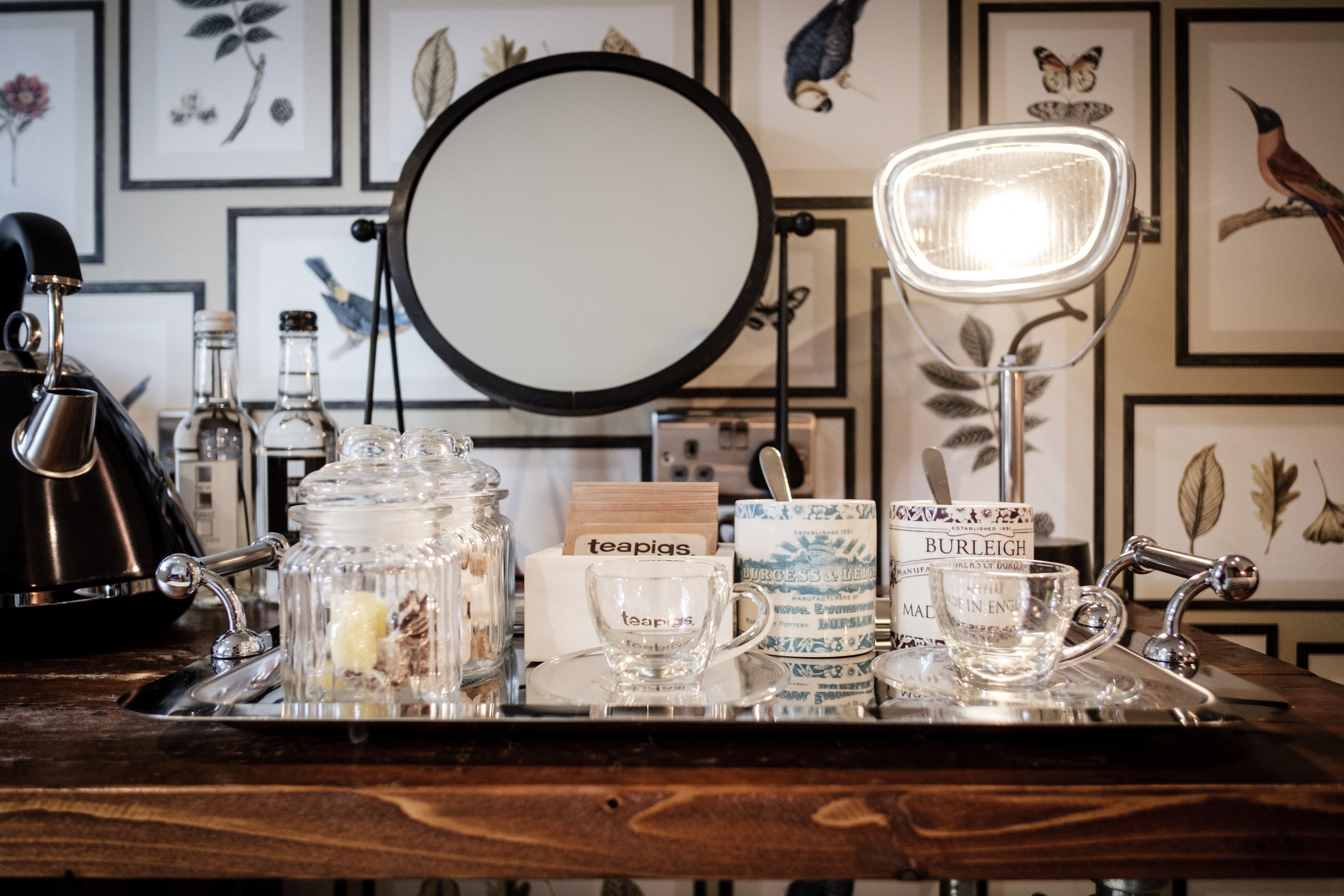 A bar area with a round mirror, a light, and various glassware and tea bags on a wooden surface.