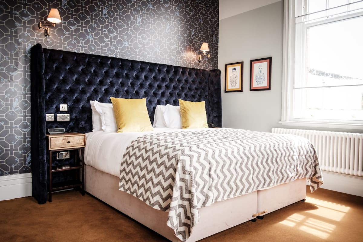 A bedroom with a tufted headboard, a bed with a patterned blanket, bedside lamps, a nightstand, and a window with a view.