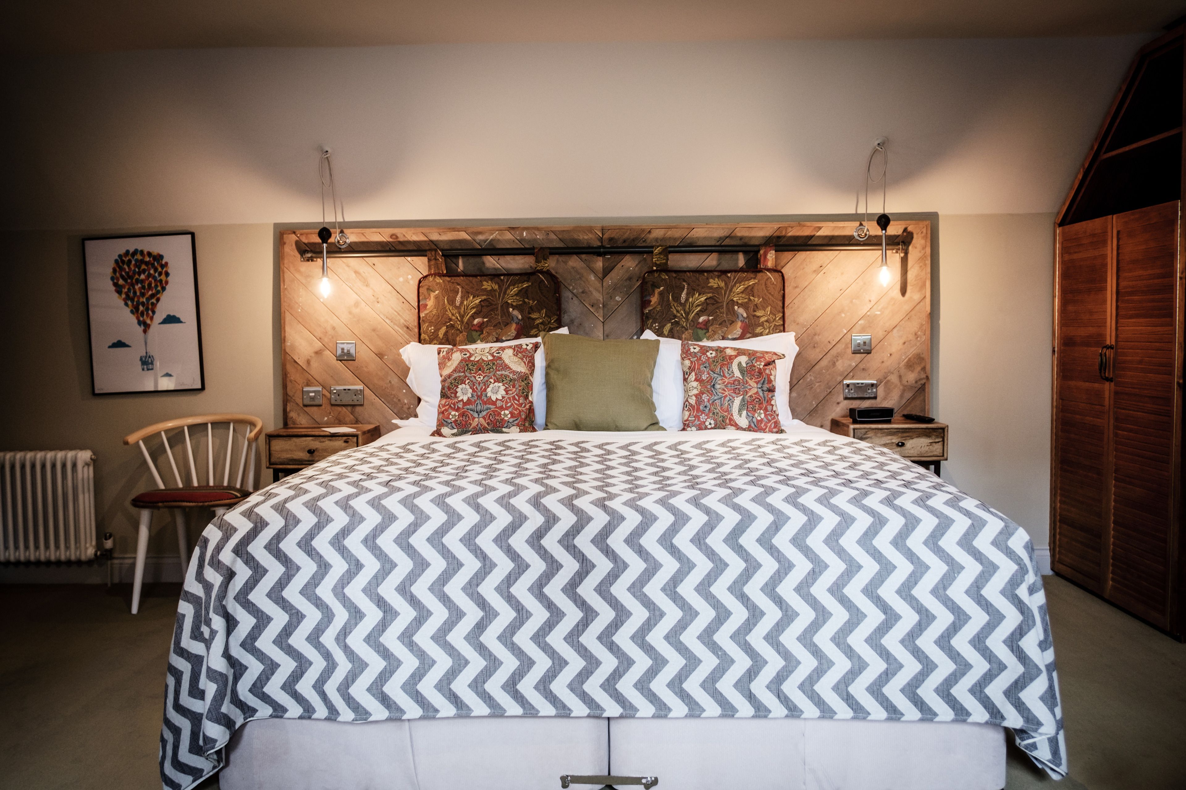 Quarto com uma cama grande, cabeceira de madeira, duas mesas de cabeceira, um criado-mudo, uma cadeira e um guarda-roupa.