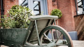 A rustic wooden cart with wheels, positioned in front of a brick building with a blue door and a small potted plant beside it.