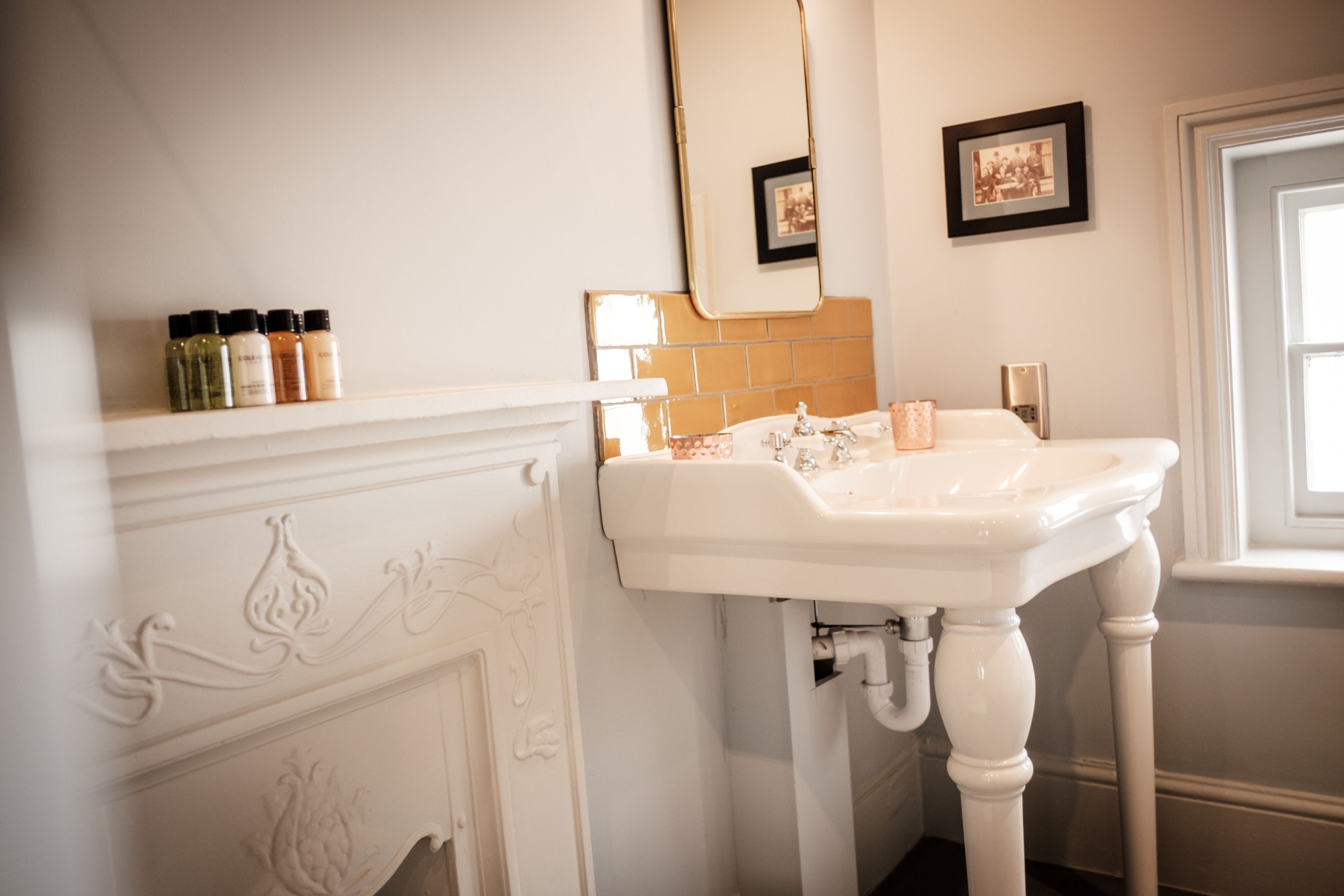 A bathroom with a white sink, decorative moldings, a mirror, and a shelf with toiletries.