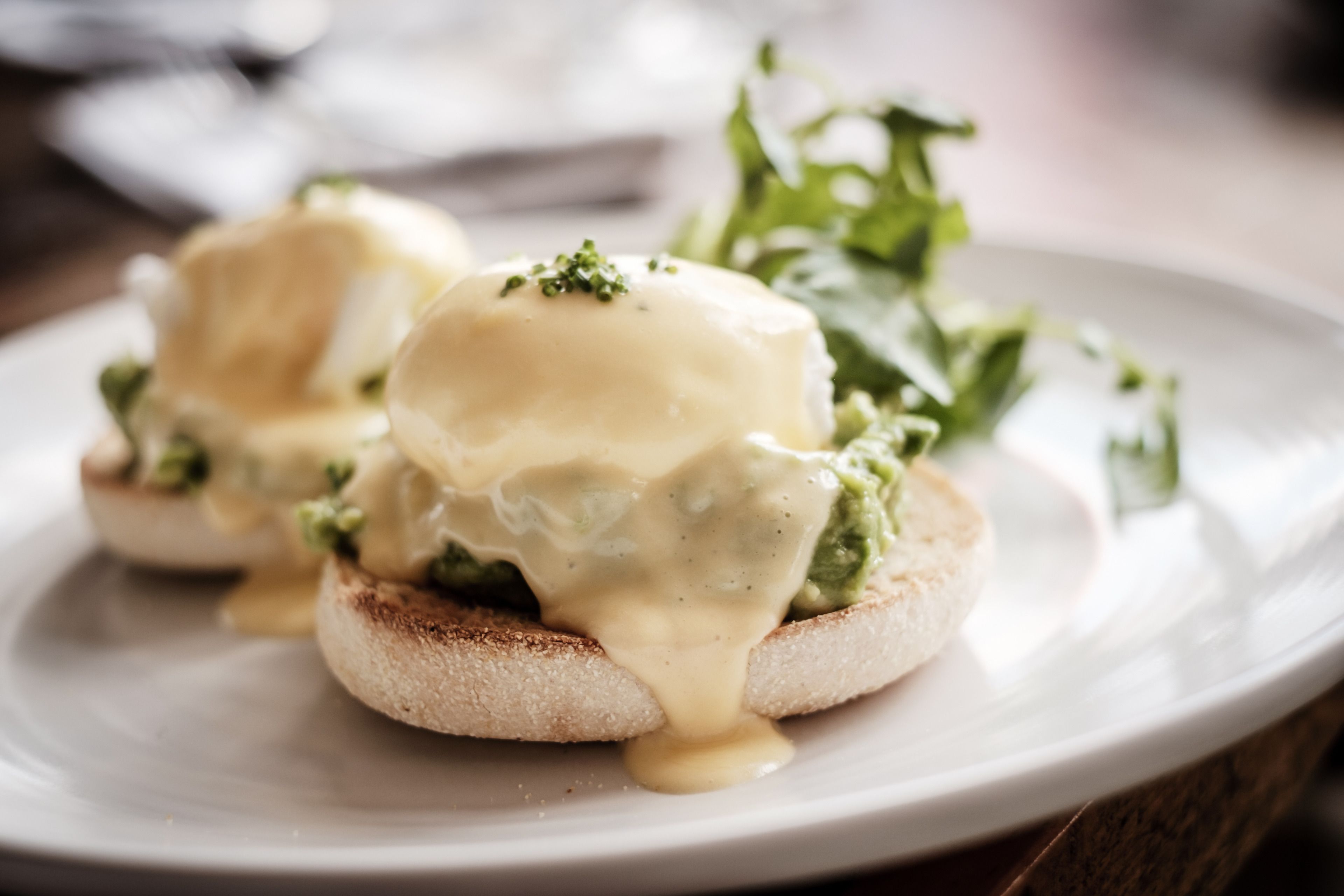 Lautasella on kaksi Eggs Benedict -leipää, ja ne on koristeltu vihreillä yrteillä. Lautanen on valkoinen.
