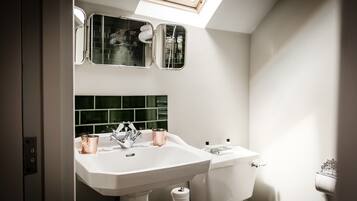 A bathroom with a white sink, two mirrors, a green-tiled backsplash, and a skylight.