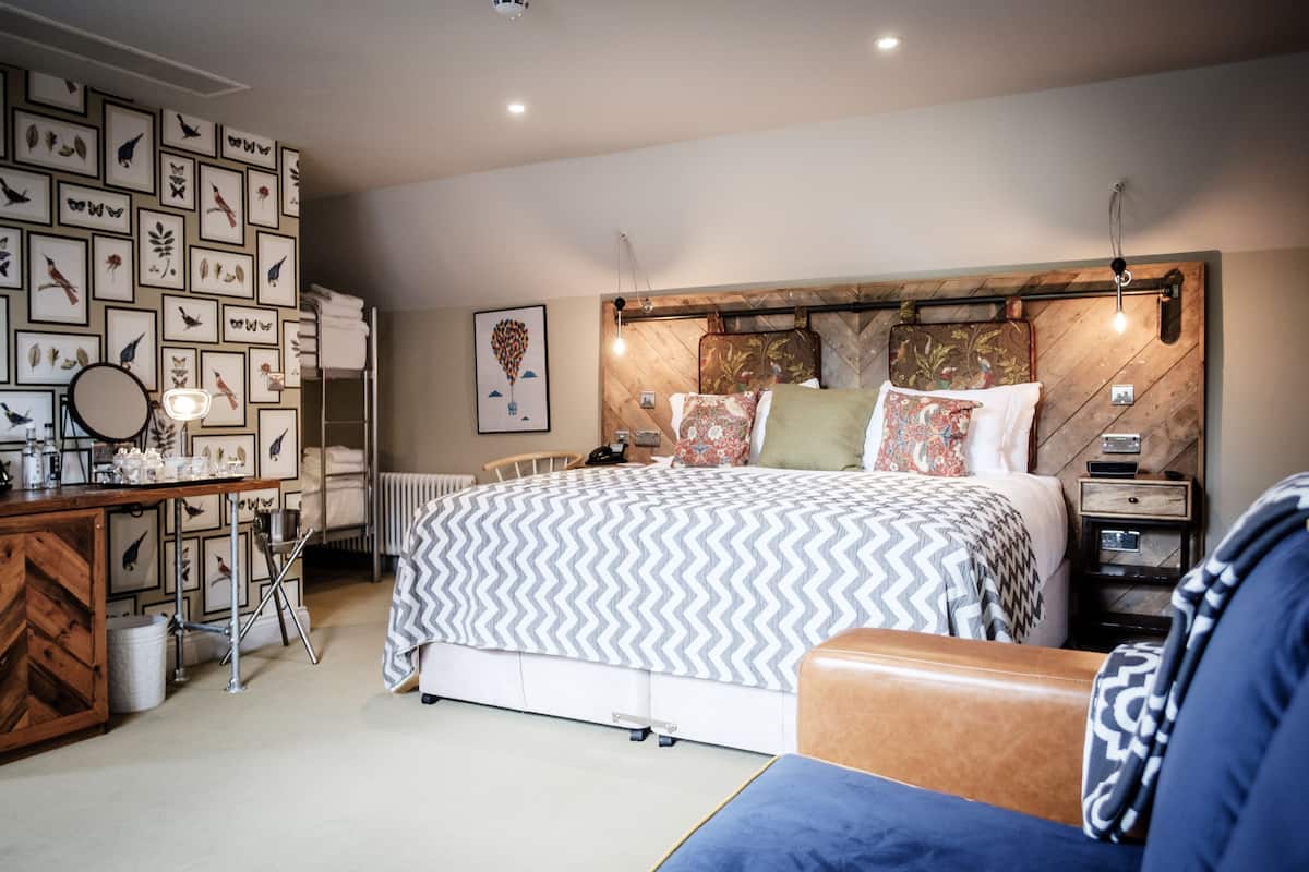 A modern bedroom with a large bed, a bedside table, a dresser, and a wall decorated with framed pictures.