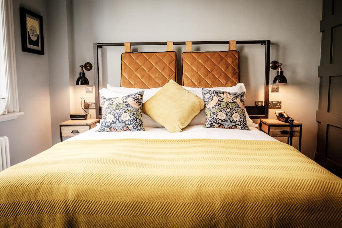 A neatly made bed with a yellow bedspread, two wooden headboards, and patterned pillows.