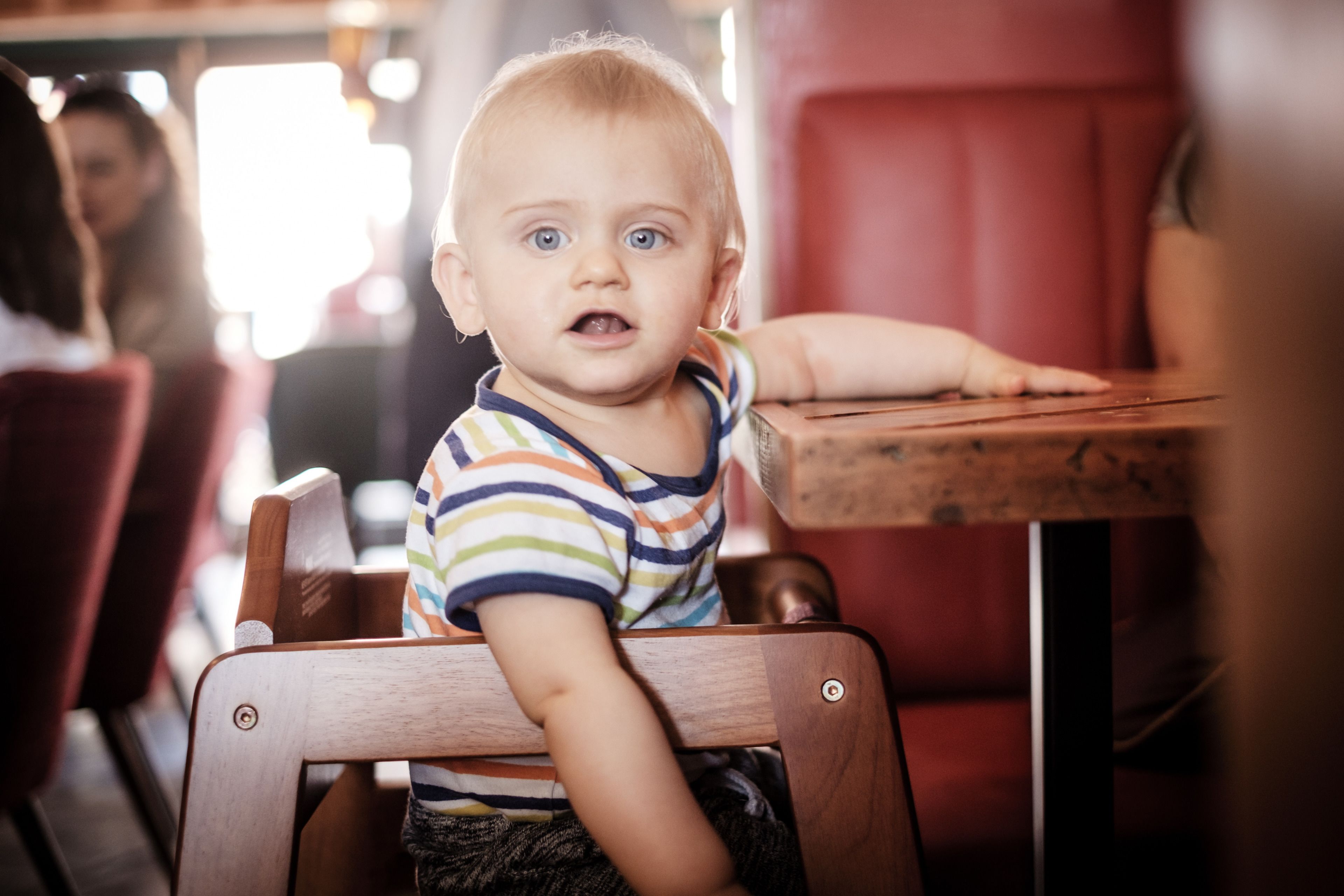 Un enfant assis sur une chaise en bois, portant un t-shirt à rayures.