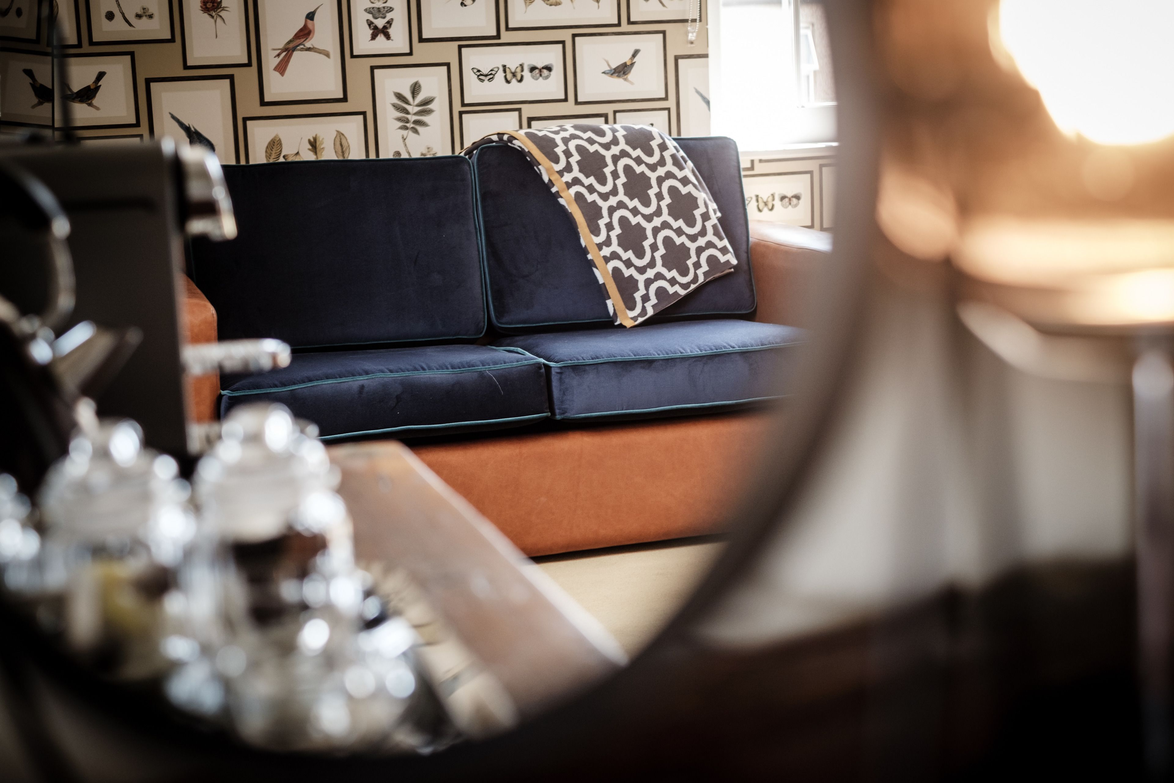 A room with a dark blue sofa, a patterned throw blanket, and a wall decorated with framed botanical prints.