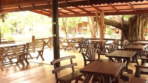 Un espacio al aire libre con mesas y bancos de madera, rodeado de árboles y un suelo de baldosas.