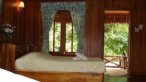 Una habitación de madera con una cama, una ventana con cortinas florales y vistas a la vegetación.
