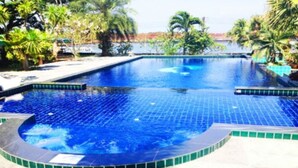 Piscina de borde curvo, rodeada de palmeras y vista a una masa de agua.