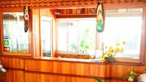 Zona de recepción con mostrador de madera, ventana con vistas a follaje y una planta en maceta.