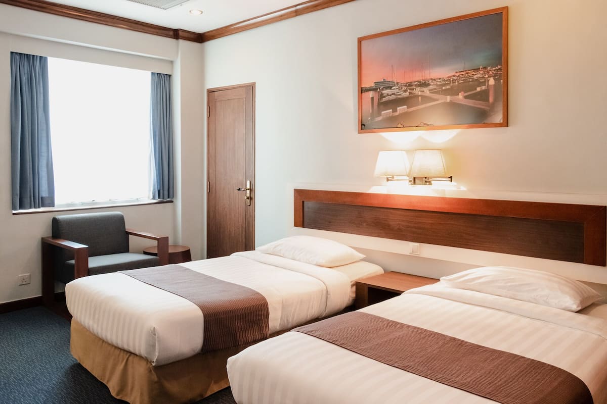 Una habitación de hotel con dos camas, un escritorio, una silla, una ventana con cortinas y un cuadro en la pared.