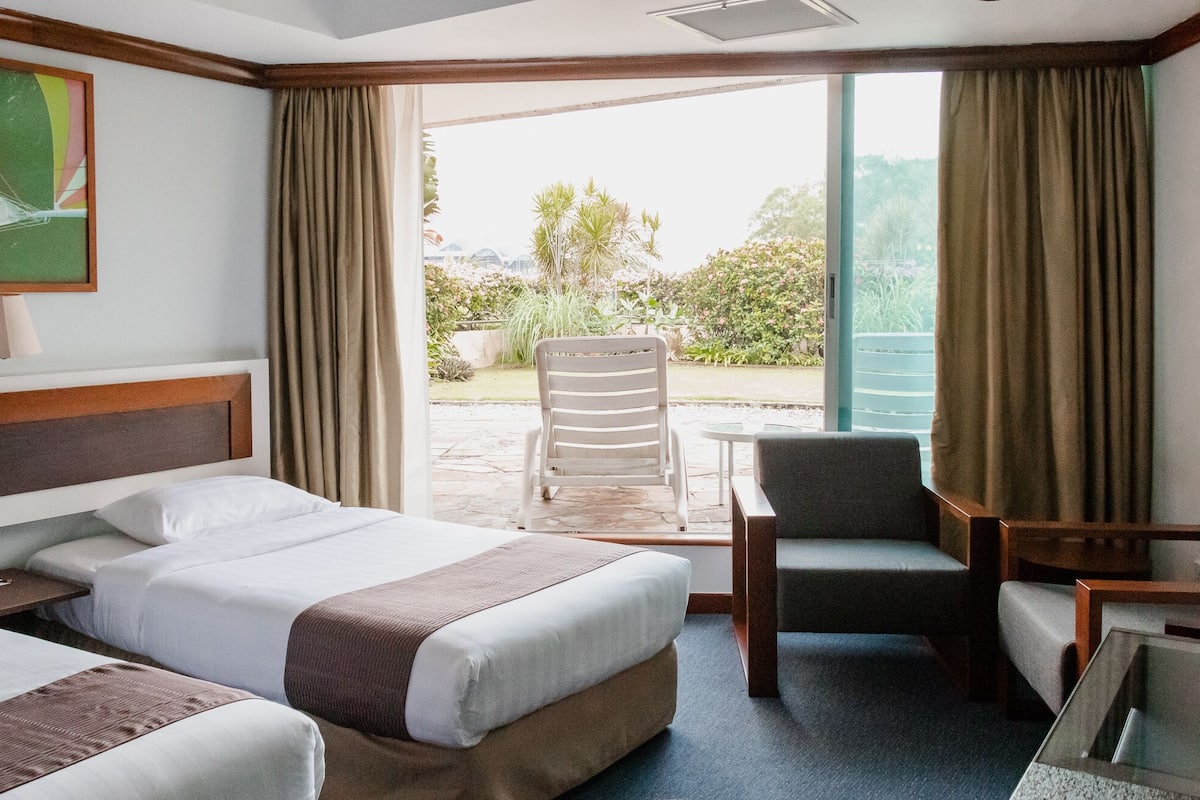 Habitación de hotel con dos camas, una silla, una mesita y vistas al exterior.