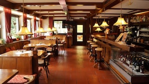 Een restaurant met houten tafels en stoelen, een bar met krukjes, en een presentatie van flessen.