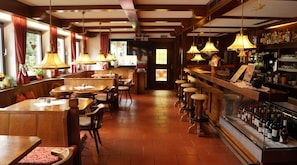 Un restaurant avec des tables et des chaises en bois, un coin bar avec des tabourets et un présentoir à bouteilles.
