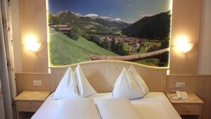 Een hotelkamer met een groot bed, twee nachtkastjes en uitzicht op een bergachtig landschap.