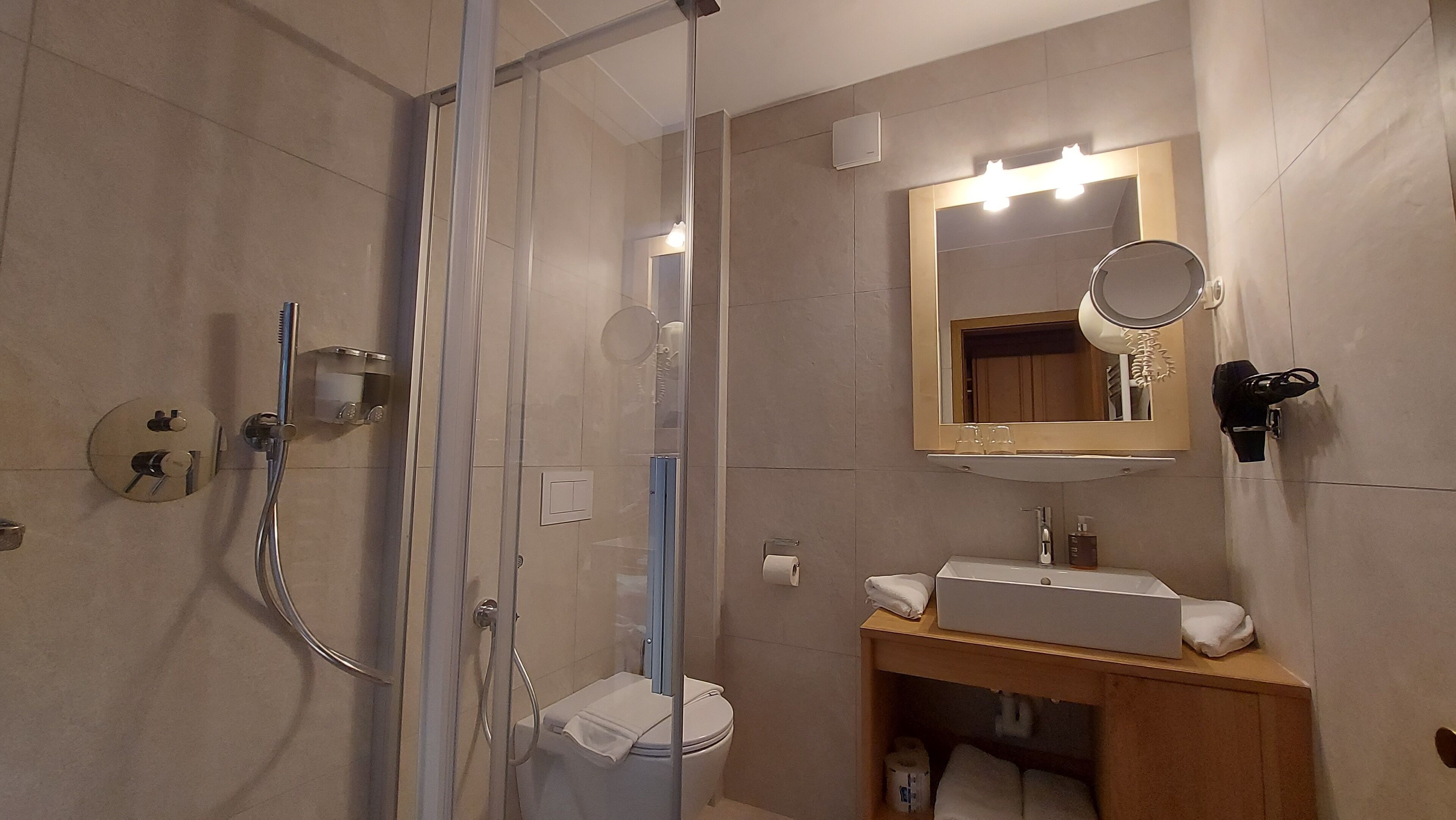 A bathroom with a glass shower enclosure, a toilet, a sink with a mirror above it, and a vanity with a towel rack.