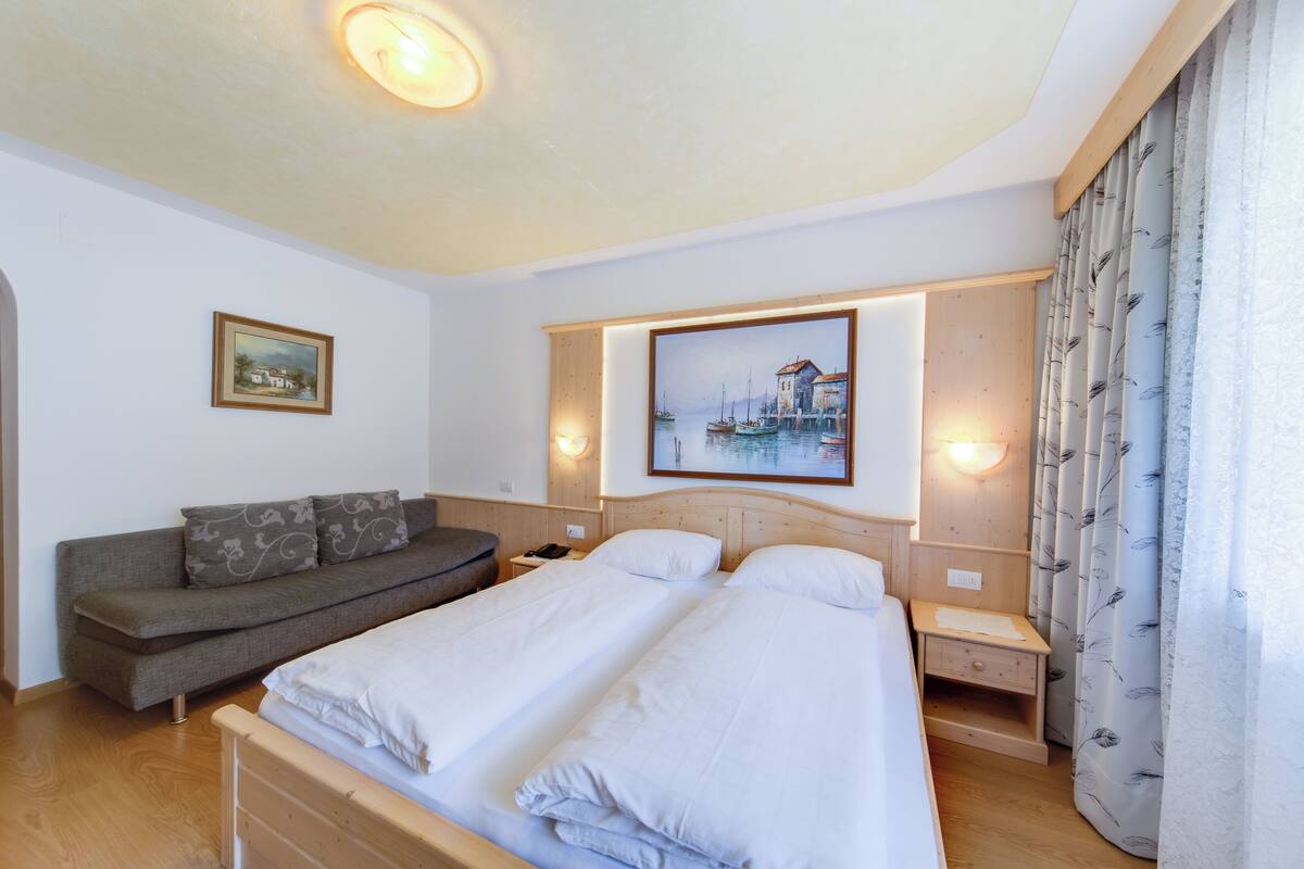 Un dormitorio con una cama doble, un sofá, una mesita de noche y una lámpara de pared.
