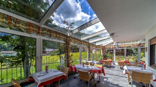 Een restaurant met terras, grote ramen en uitzicht op een groen landschap.
