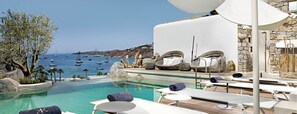 Un área junto a la piscina con sillones de descanso, vista al mar y un muro de piedra.