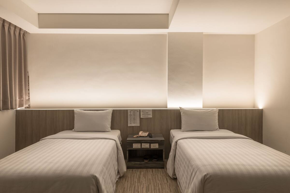 Ein Hotelzimmer mit zwei Einzelbetten, einem Nachttisch mit Telefon und Lampe sowie einem Holzkopfende.