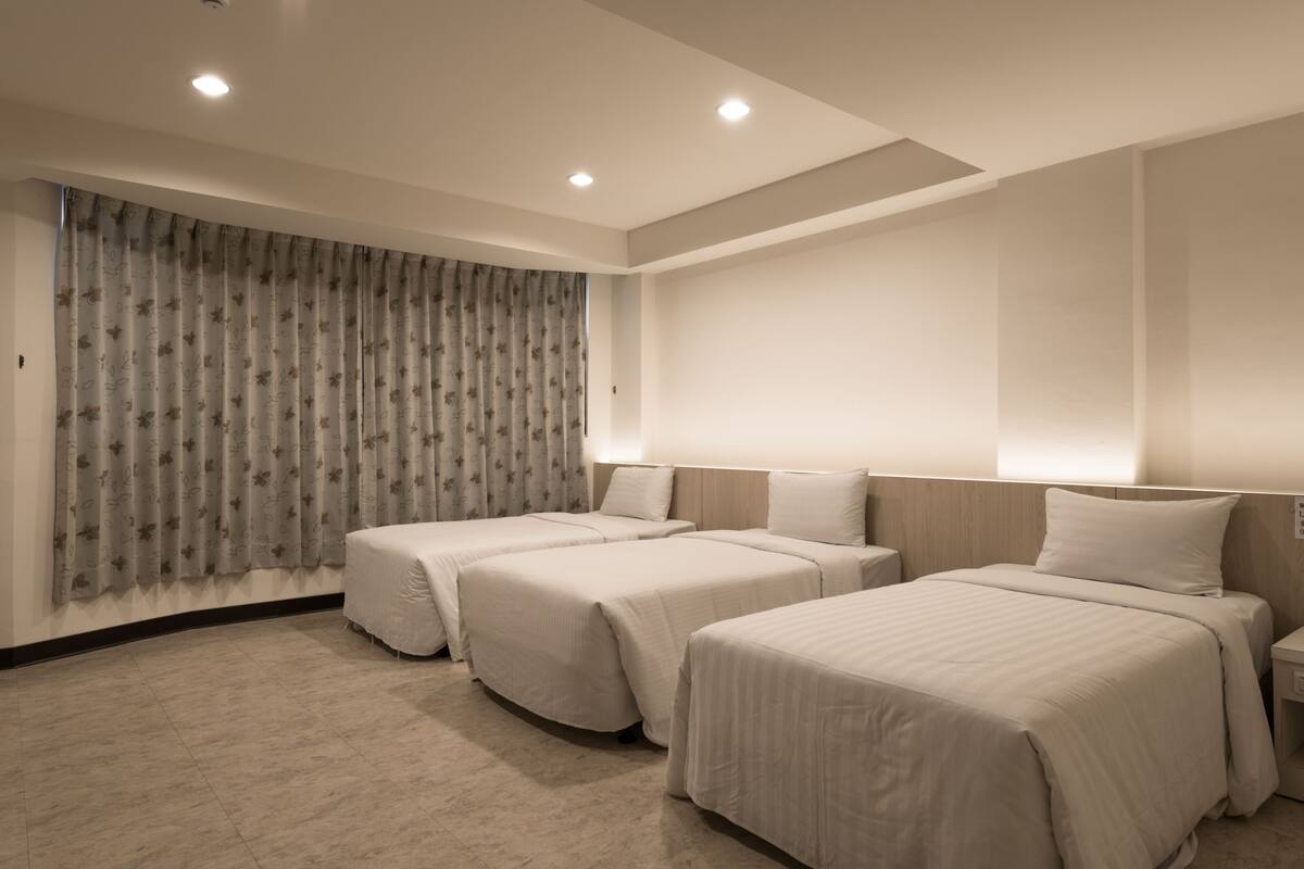 Ein Hotelzimmer mit zwei Einzelbetten, einem großen Fenster mit Vorhängen und einer neutralen Farbgestaltung.