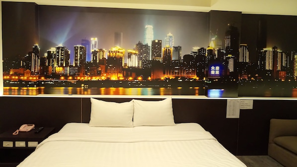Habitación de hotel con amplia vista panorámica de la ciudad, cama con ropa blanca, mesita de noche con teléfono y una silla.