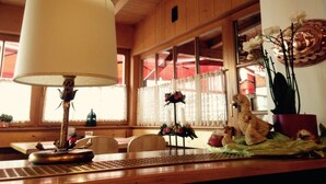 A wooden interior with a table lamp, a window with curtains, and decorative items including a bird sculpture and orchids. - Hotel Ristorante Walter (San Candido)