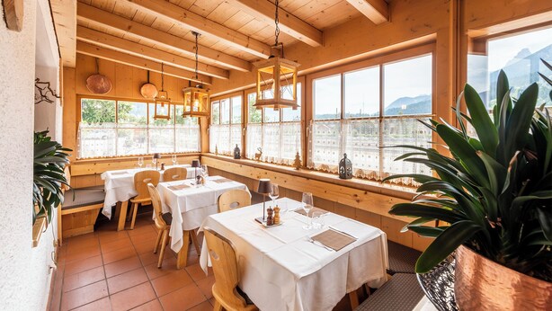 A restaurant with wooden interiors, large windows, and a view of mountains. Tables are set with white tablecloths and wine glasses. - Hotel Ristorante Walter (San Candido)