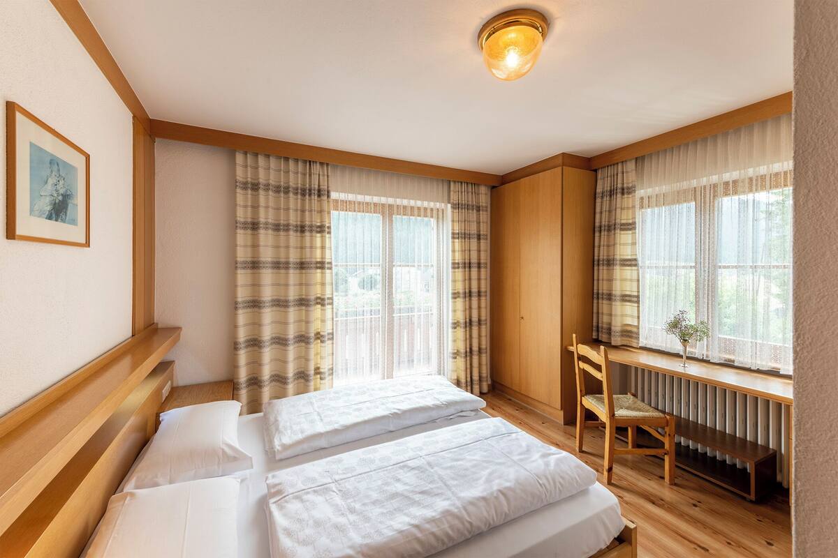 A bedroom with two beds, a wooden desk, and a chair.
