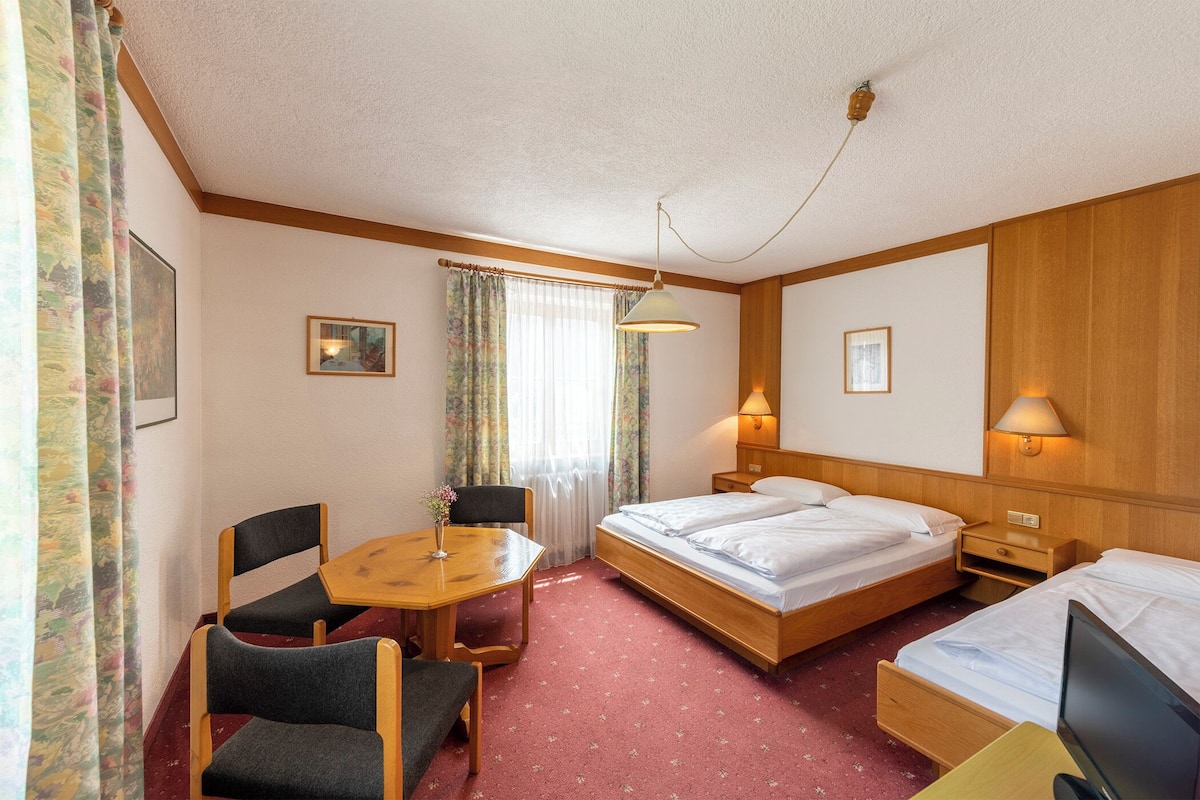 A hotel room with a wooden bed, a desk with two chairs, a table, and a TV.