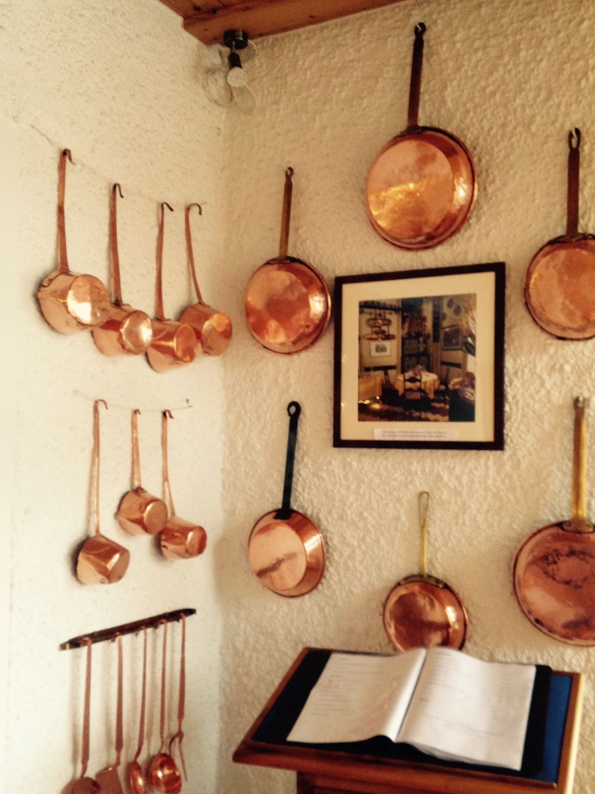 Une cuisine avec des ustensiles de cuisine en cuivre accrochés au mur et une photo encadrée.
