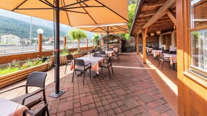 An outdoor patio with tables and chairs, covered by large umbrellas, and a view of the mountains in the background. - Hotel Ristorante Walter (San Candido)