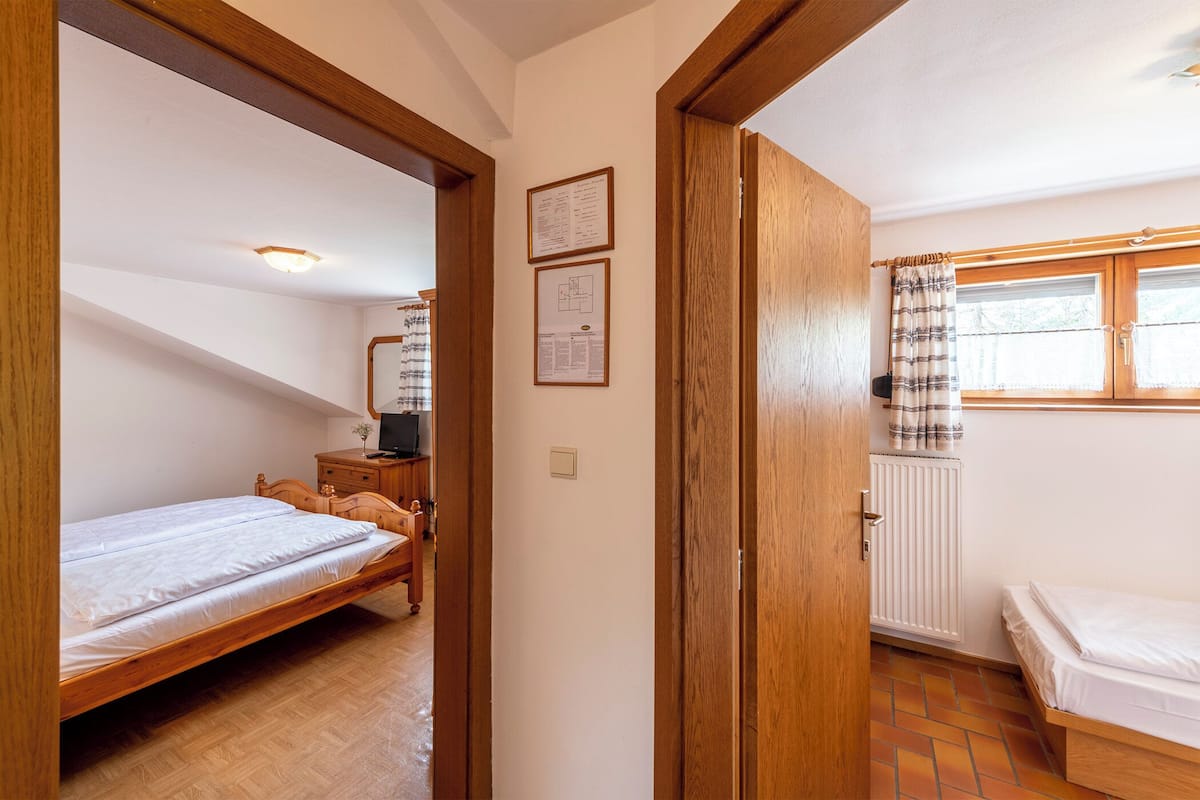A bedroom with two beds, wooden flooring, a radiator, and a window with curtains.