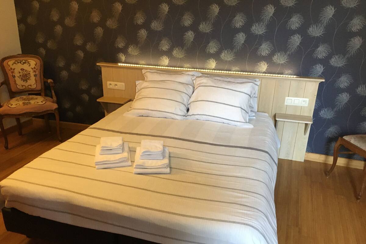 A neatly made bed with striped bedding, two pillows, and two folded towels on the foot of the bed.