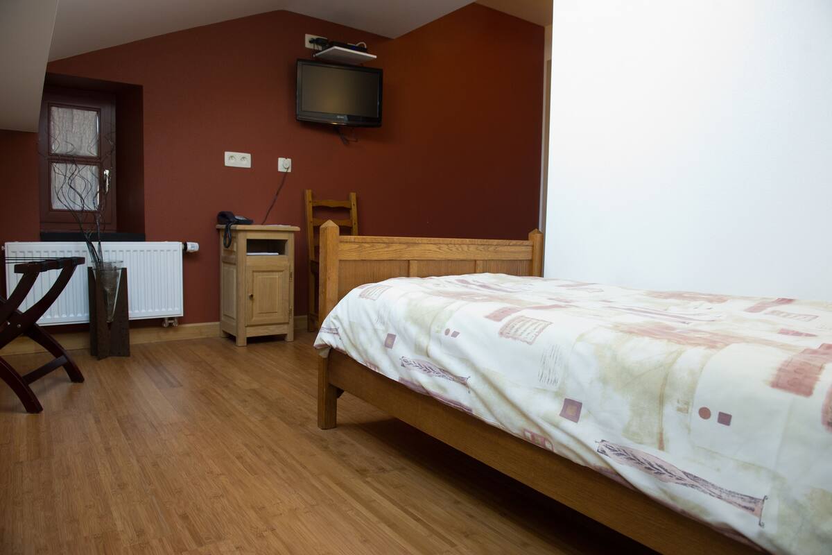 A bedroom with a wooden bed, a desk, a chair, a radiator, and a television mounted on the wall.